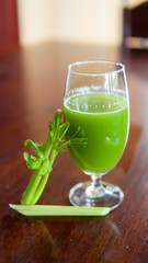Fresh green celery juice in glass on wooden brown background