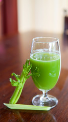 Fresh green celery juice in glass on wooden brown background