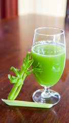 Fresh green celery juice in glass on wooden brown background