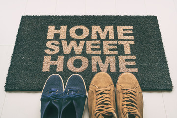 Door mat Shoes at front entrance of condo apartment. Written welcome sign Home Sweet Home welcoming...