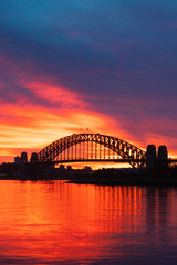 Silhouette of Sydney Harbour Bridge with orange burning sky at dawn.