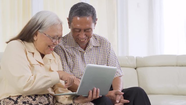 Happy senior couple using a laptop computer together while sitting on the sofa at home. Shot in 4k resolution