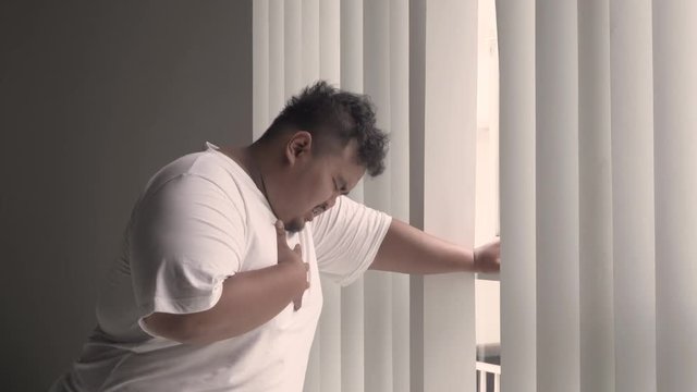 Overweight man feels heart attack while standing near the window at home. Shot in 4k resolution
