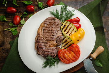 Grilled meat steak with zucchini, dill and tomatoes. Cafe menu on a wooden background in warm colors with copy space.