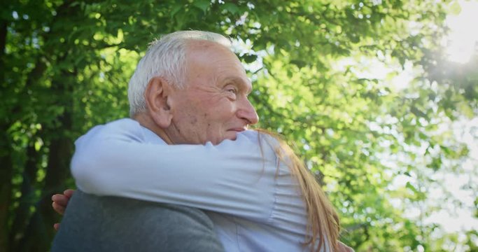 Slow motion of happy granddaughter is giving an effective hug to her grandfather as a sign of love and respect in a green park on a sunny day.