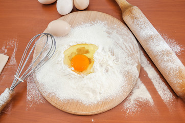 The concept of making dough. Egg chicken  in flour, wooden spatula, whisk and rolling pin on a wooden table.