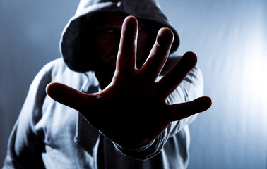 A hooded man holds his hand in front of his face defensively. Concept self-defense.