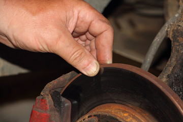 Checking the thickness of the brake disk, car service - close up hand points your fingers at...