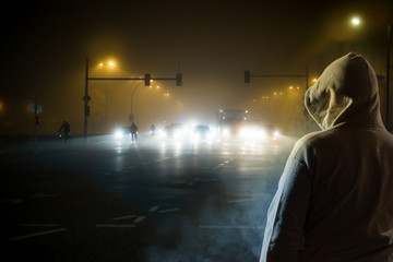 A man is waiting at night at a street. In the haze you can see cars and cyclists. Concept road traffic.
