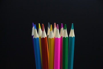 Close-up of a bunch of upright new colored pencils in the center of black background space