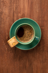A cup of black coffee with a cookie on a dark rustic wooden background, shot from above with a place for text