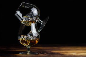 Two whiskey / cognac glasses with ice on a wooden background. Dark backdrop.