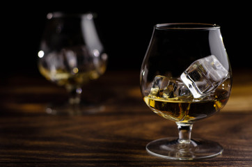 Two whiskey / cognac glasses with ice on a wooden background. Dark backdrop.