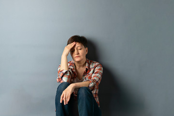Portrait of a young woman with a short haircut who is sitting against the wall on gray empty...