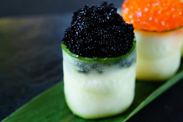 Red and tobiko caviar topped sushi rolls set with philadelphia cream cheese on bamboo leave,...