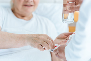 partial view of doctor giving medicine and glass of water to patient