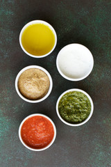 Set of sauces on dark green background. Marinara or tomato sauce, yogurt, pesto, olive oil and mustard