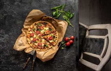 on a dark, stone table stands an old frying pan with pizza in baking paper. Baked and crunchy pizza...
