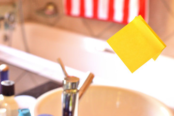 Piece of square yellow sheet use to give notation stick to washroom mirror