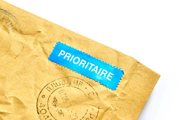 Closeup of brown envelope isolated on white with blue prioritaire mail or priority mail sticker and round stamp