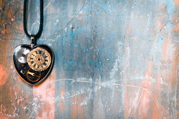 on the old ancient wall there is a pendant in the shape of a heart on a rope, and inside it is an old clock mechanism; concept photo show that eternal love is timeless