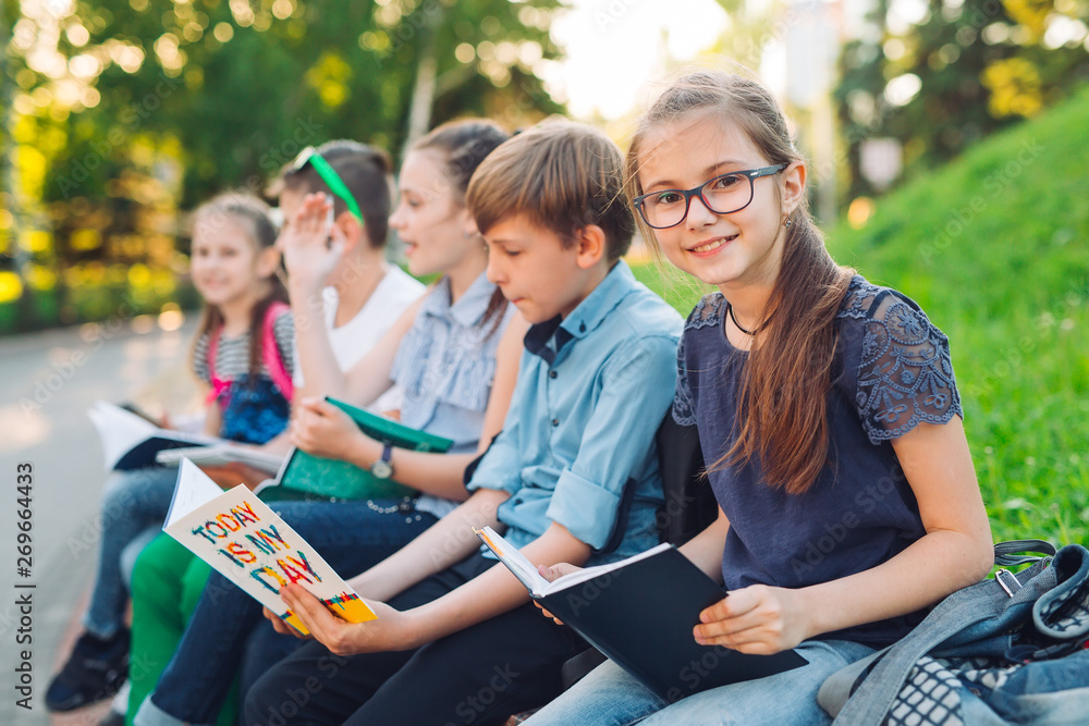 Wall mural happy schoolmates portrait. schoolmates seating with books in a wooden bench in a city park and stud