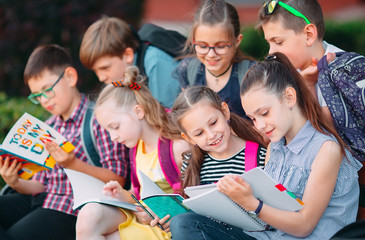 Happy Schoolmates Portrait. Schoolmates seating with books in a wooden bench in a city park and studying on sunny day.