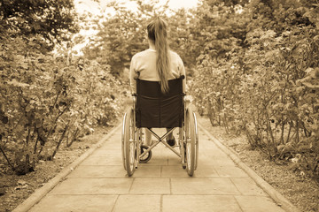 Young girl in wheelchair seen from behind. Outdoors, in a park