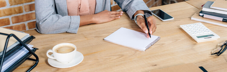 panoramic shot of african american Casual businesswoman writing in notebook at desk