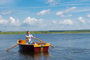 a man in yellow glasses, sailing on a boat with a fishing rod and oars to catch big fish, against a beautiful landscape