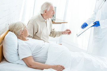 Obraz premium partial view of doctor holding clipboard, sick patient and senior man in clinic