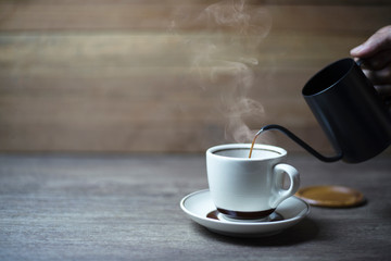 Coffee time, Black coffee in a kettle that is pouring into the cup, Put on wooden table, Copy-space.