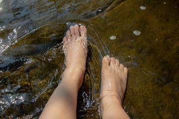 Woman relaxing.Dipping feet in water with rock at the background.