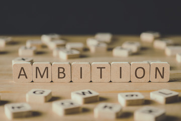 selective focus of cubes with word ambition surrounded by blocks with letters on wooden surface isolated on black