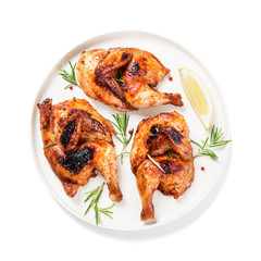 Halves of appetizing grilled juicy chicken with golden brown crust served with lemon slices,barbeque  sauce and rosemary. isolated on white background