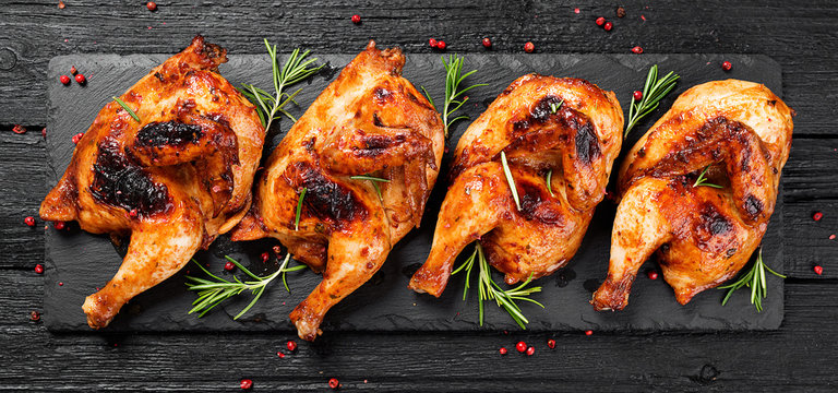 Halves of appetizing grilled juicy chicken with golden brown crust served with lemon slices,barbeque  sauce and rosemary. - Powered by Adobe