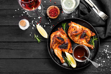 Halves of appetizing grilled juicy chicken with golden brown crust served with lemon slices,barbeque  sauce and rosemary.
