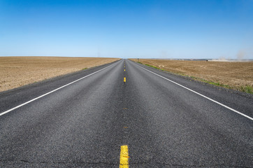 empty highway with a farm tractor in the fields