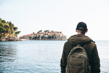 TView of the island of Sveti Stefan in Montenegro. The tourist looks at it. Selective focus. The man is blurred.