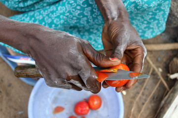 Close-up of Tanzanian woman cutting tomatoes for traditional meal in a rural village on Ukerewe...
