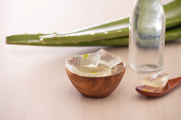 Bowl with peeled aloe vera and green leaves on wooden background