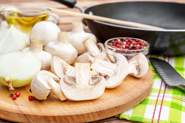 Cooking food. Cutting board with champignons, onion and spices and frying pan on the table.