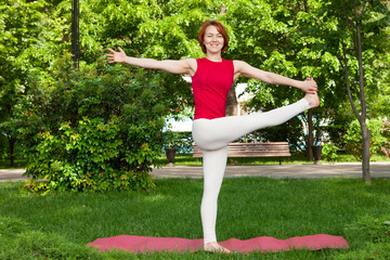 Smiling girl in the park exercise on the yoga mat, high lunge