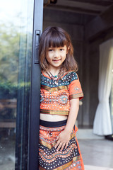 Authentic  portrait of pretty thai baby girl posing outdoors, dressed in traditional colorful dress, jewelry, being in good mood,smiling and looking at camera. Attractive child enjoying life