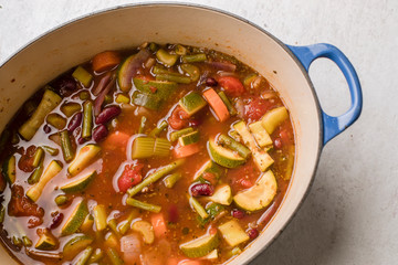 Top view of homemade vegetarian organic minestrone in a blue Dutch oven pot. Overhead, close up. 