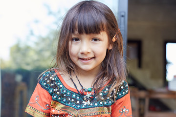 Authentic  portrait of pretty thai baby girl posing outdoors, dressed in traditional colorful dress, jewelry, being in good mood,smiling and looking at camera. Attractive child enjoying life