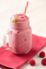Healthy frozen strawberry and raspberry smoothie in a mason jar glass with a straw, fresh mint and scattered berries over a pink napkin and light background