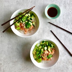 Top view of two Poke bowls with raw marinated salmon, cilantro, avocado, cucumber , sesame seeds and rice noodles served with soy/tamari sauce and wooden chopsticks. Flat lay on light background. 