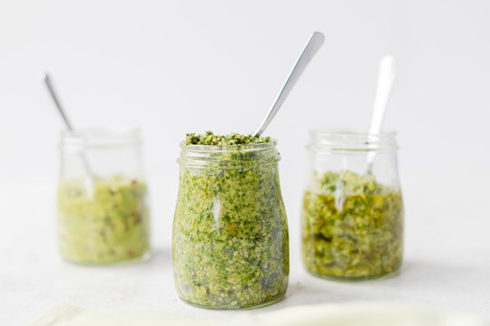 Three pestos in glass jars: avocado, hemp seeds and pumpkin seeds pesto; almond, mint and basil pesto: walnut, kale and parsley pesto served with a spoon on light background. Horizontal, copy space.