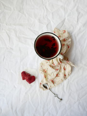 Obraz na płótnie Canvas Tea concept. White cup of hibiscus tea and raspberry candy от a linen tablecloth.Kinfolk and comfort food atmosphere concept